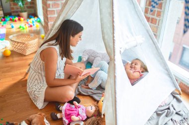 Anaokulunda Tip 'in içinde yerde yatan sarışın kıza güzel bir öğretmen kitabı okuyor.