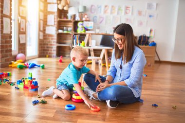 Genç beyaz çocuk öğretmeniyle oyun okulunda oynuyor. Anne ve oğlu, istihbarat oyuncağıyla oyun odasında.
