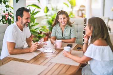 Güzel bir aile terasta oturmuş kahve içiyor, konuşuyor ve gülümsüyor.