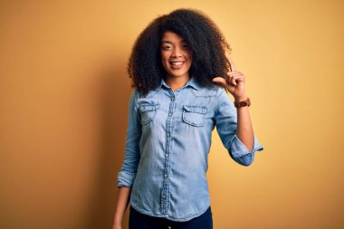 Sarıya boyanmış arka planda duran, gülümseyen ve el hareketleriyle küçük boy işareti yapan, parmaklarıyla kameraya bakan Afro saçlı, güzel Afrikalı Amerikalı bir kadın. Ölçü kavramı.
