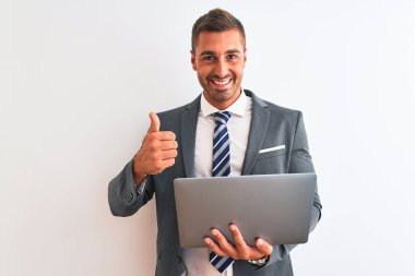 Genç yakışıklı iş adamı bilgisayarını kullanarak izole edilmiş arka planda çalışıyor. Kocaman gülümsüyor. Tamam işareti yapıyor.