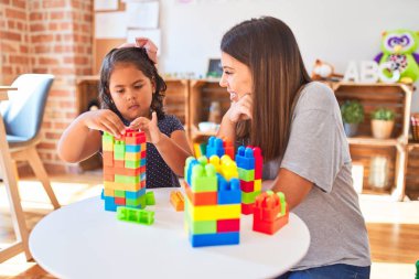 Güzel öğretmen ve küçük kız anaokulunda inşaat bloklarıyla oynuyorlar.