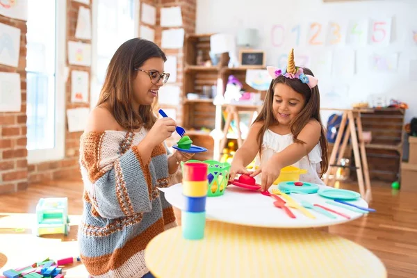 幼稚園のおもちゃの周りのプラスチック製の食べ物やカトラリーを使用して幸せな遊びの食事を笑顔で美しい先生と幼児 — ストック写真
