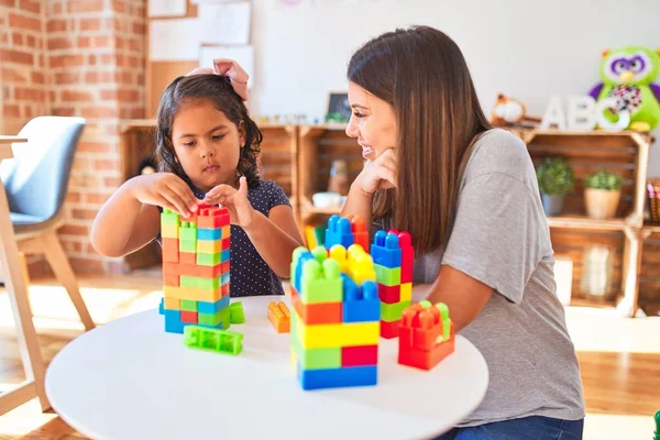 Güzel öğretmen ve küçük kız anaokulunda inşaat bloklarıyla oynuyorlar.