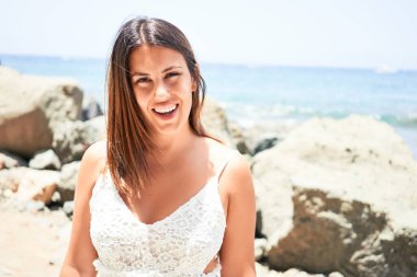 Güzel genç bir kadın kumsalda yürüyor okyanus manzarasının tadını çıkarıyor yaz tatilinde gülümsüyor.