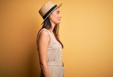 Young beautiful brunette woman on vacation wearing casual dress and hat looking to side, relax profile pose with natural face with confident smile.