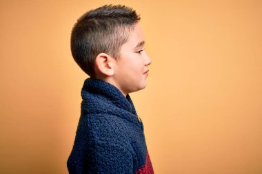 Young little boy kid wearing winter sweater over yellow isolated background looking to side, relax profile pose with natural face with confident smile.