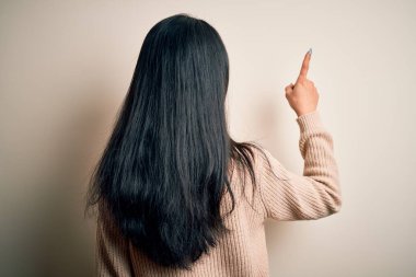 Young beautiful chinese woman wearing casual sweater over isolated white background Posing backwards pointing ahead with finger hand