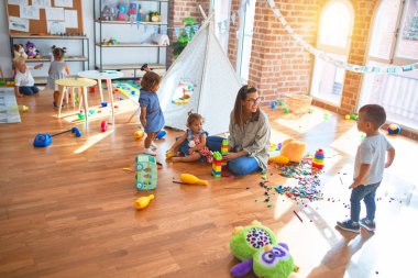 Güzel öğretmen ve bir grup çocuk anaokulunda bir sürü oyuncakla oynuyorlar.