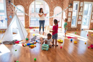 Anaokulunda bir sürü oyuncağın etrafında basketbol oynayan genç ve güzel öğretmenler ve yeni yürümeye başlayan çocuklar.