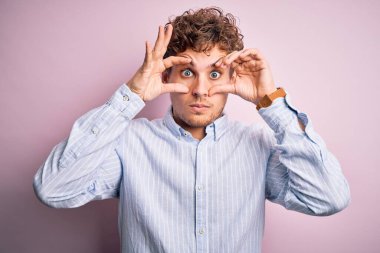 Young blond handsome man with curly hair wearing striped shirt over white background Trying to open eyes with fingers, sleepy and tired for morning fatigue