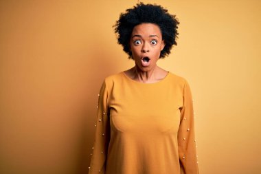 Kıvırcık saçlı, sıradan tişörtlü, genç, Afro-Amerikan bir kadın. Sürpriz bir ifadeden, korkudan ve heyecanlı bir surattan korkuyor ve şok oluyor..