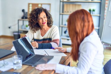 Birlikte çalışan mutlu ve kendinden emin gülümseyen iki güzel iş kadını. Ofiste gülümseyen bir gülümsemeyle oturuyor.