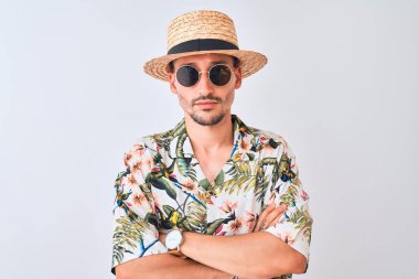 Young handsome man wearing Hawaiian shirt and summer hat over isolated background skeptic and nervous, disapproving expression on face with crossed arms. Negative person.