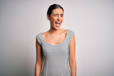 Young beautiful brunette woman wearing casual striped dress over isolated white background winking looking at the camera with sexy expression, cheerful and happy face.