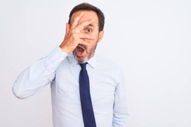 Middle age businessman wearing elegant tie standing over isolated white background peeking in shock covering face and eyes with hand, looking through fingers with embarrassed expression.