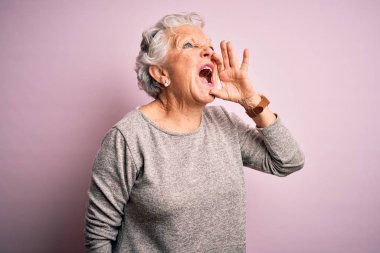 Senior beautiful woman wearing casual t-shirt standing over isolated pink background shouting and screaming loud to side with hand on mouth. Communication concept.