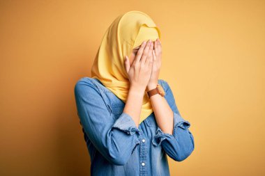 İzole edilmiş sarı arka planda duran Müslüman başörtüsü takan genç ve güzel bir kız. Ağlarken yüzünü ellerle kapatan üzgün bir ifade. Depresyon kavramı.
