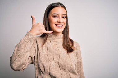 Genç, güzel, esmer bir kadın beyaz arka planda dikilmiş telefonda el ve parmaklarıyla telefonla konuşurken gülümsüyor. İletişim kavramları.