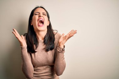 Mavi gözlü genç esmer kadın izole edilmiş beyaz arka plan üzerine gündelik süveter giyerek başarının çılgınlığını kollarını kaldırarak ve gözlerini kapayarak heyecanla bağırarak kutluyor. Kazanan konsept