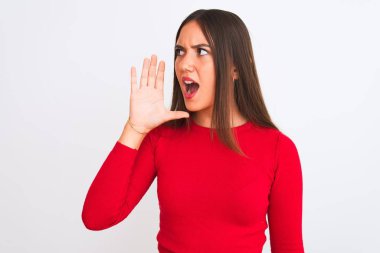 Young beautiful girl wearing red casual t-shirt standing over isolated white background shouting and screaming loud to side with hand on mouth. Communication concept.