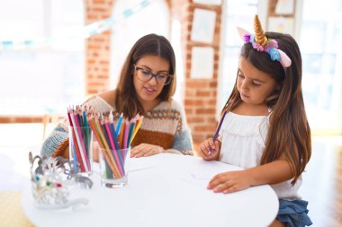 Anaokulundaki bir sürü oyuncağın etrafına kağıt ve kalem kullanarak tek boynuzlu at resmi çizen güzel öğretmen ve çocuk.