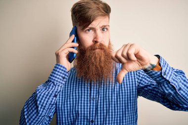 Kızıl saçlı, sakallı bir İrlandalı adam, izole bir arka planda akıllı telefondan konuşuyor. Sinirli bir yüz ifadesi var. Negatif işaretler, baş parmakları aşağıda, reddedilme kavramı.