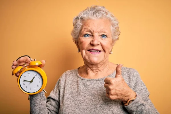 Senior Beautiful Woman Holding Alarm Clock Standing Isolated Yellow Background — Stok fotoğraf