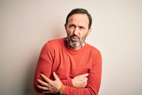 Middle age hoary man wearing casual orange sweater standing over isolated white background shaking and freezing for winter cold with sad and shock expression on face