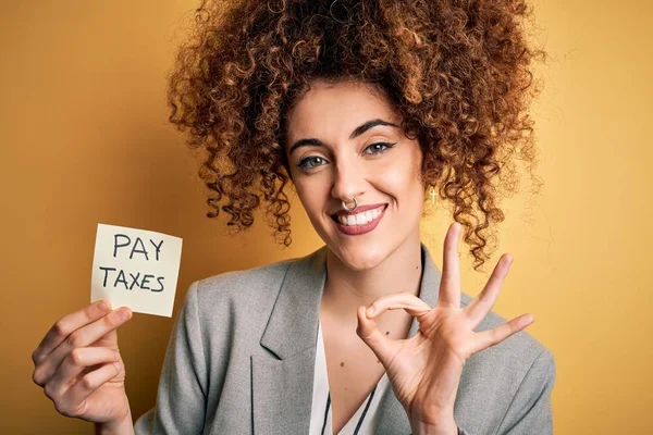 若いですビジネス女性とともに巻き毛保持は 指でOkサインを行う黄色の背景を思い出させるために税金を支払う 優れたシンボル — ストック写真