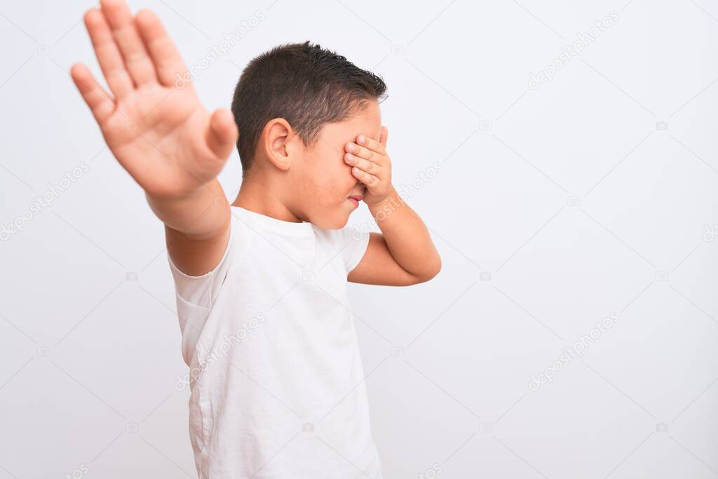 Beautiful kid boy wearing casual t-shirt standing over isolated white background covering eyes with hands and doing stop gesture with sad and fear expression. Embarrassed and negative concept.