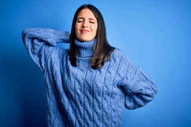 Young brunette woman with blue eyes wearing casual turtleneck sweater Suffering of neck ache injury, touching neck with hand, muscular pain