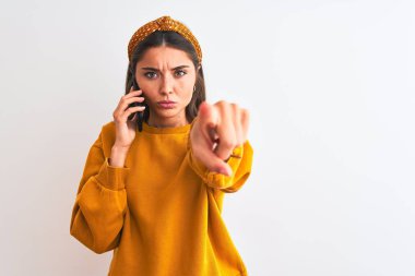 Akıllı telefonda konuşan genç ve güzel bir kadın izole edilmiş beyaz arka planda durup kamerayı işaret ediyor ve sen, el işareti, ön taraftan pozitif ve kendinden emin bir hareket.