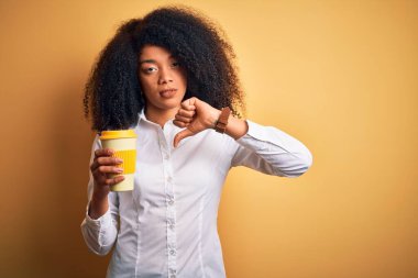 Afro saçlı, kızgın yüzlü kahve fincanından kahve içen Afro Amerikalı genç bir iş kadını. Negatif işaretler baş parmakları aşağıda, reddedilme kavramı.