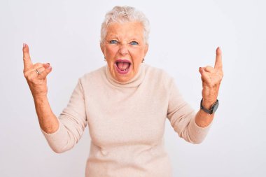 Balıkçı yaka kazak giyen yaşlı, gri saçlı kadın izole edilmiş beyaz arka planda dikiliyor çılgın bir ifadeyle elleri havada rock sembolü yapıyor diye bağırıyor. Müzik yıldızı. Ağır müzik konsepti.