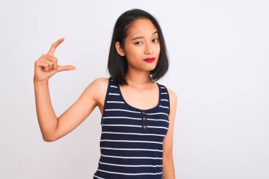 İzole edilmiş beyaz arka plan üzerinde duran çizgili tişört giyen genç Çinli kadın gülümsüyor ve el hareketleriyle küçük boy işareti yapıyor ve kameraya bakıyor. Ölçü kavramı.