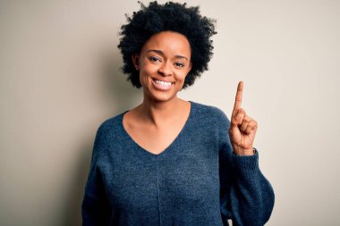 Young beautiful African American afro woman with curly hair wearing casual sweater pointing finger up with successful idea. Exited and happy. Number one.