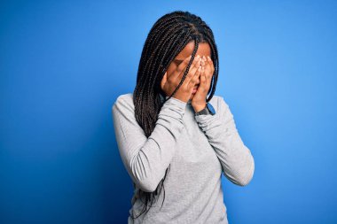 Young african american woman standing wearing casual turtleneck over blue isolated background with sad expression covering face with hands while crying. Depression concept.