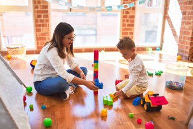 Güzel öğretmen ve bebek anaokulunda bir sürü oyuncağın etrafında yapı taşlarıyla oynuyorlar.
