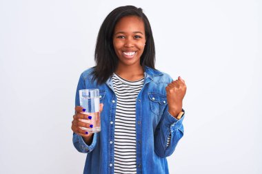 Young african american woman drinking a glass of fresh water over isolated background screaming proud and celebrating victory and success very excited, cheering emotion
