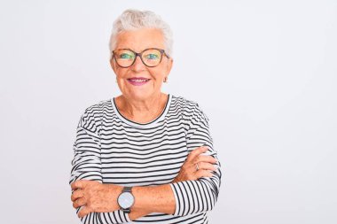 İzole edilmiş beyaz arka plan üzerinde çizgili donanma tişörtü gözlüğü takan yaşlı gri saçlı kadın kameraya bakarken kollarını kavuşturup gülümsüyor. Pozitif kişi.
