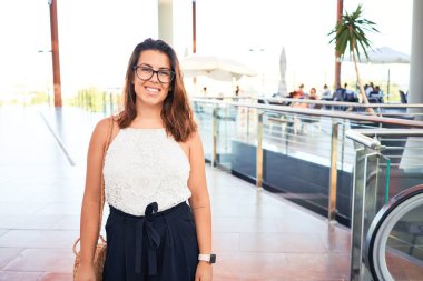 Alışveriş merkezinin içinde mutlu ve neşeli bir şekilde duran genç ve güzel bir kadın.