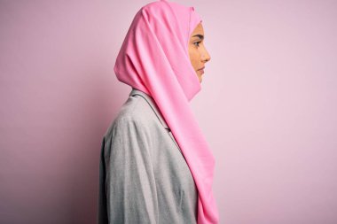 Pembe Müslüman başörtüsü ve iş ceketi giyen genç, güzel, esmer iş kadını. Taraf arıyor, rahat poz veriyor, kendine güvenen bir gülümseme takınıyor..