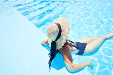 Tatil günü havuzda yüzen, güneşli bir günde suda güneşlenen güzel ve seksi bir kadın.