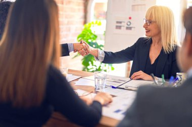 Bir grup iş adamı mutlu ve kendinden emin gülümsüyor. Ofiste anlaşmak için gülümseyerek el sıkışıyoruz.