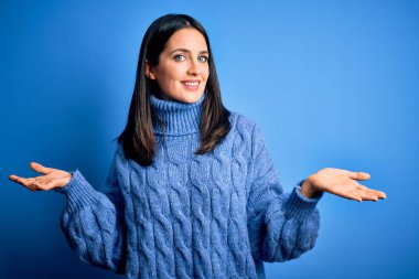 Young brunette woman with blue eyes wearing casual turtleneck sweater smiling showing both hands open palms, presenting and advertising comparison and balance