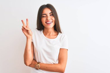 İzole edilmiş beyaz arka plan üzerinde sıradan tişört giyen genç ve güzel bir kadın kameraya gülümseyip parmaklarıyla zafer işareti yapıyor. İki numara..