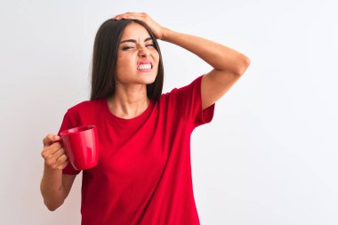 İzole edilmiş beyaz arka planda duran kırmızı fincan kahve içen genç ve güzel bir kadın. Elleri başının üstünde, utanç ve şaşkınlık dolu, sinirli ve hayal kırıklığına uğramış bir halde. Hata için korku ve üzüntü.