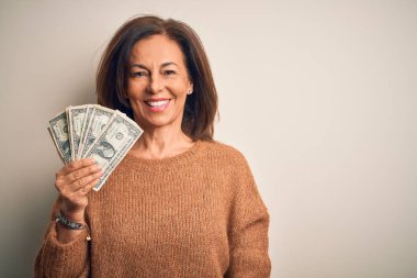 Middle age brunette woman holding one dollars bank notes over isolated background with a happy face standing and smiling with a confident smile showing teeth