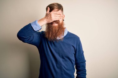 Yakışıklı, kızıl saçlı, sakallı bir iş adamı izole edilmiş arka planda duruyor. Gülümsüyor ve yüzünde şaşkınlıktan gözleri kapayarak gülüyor. Kör kavram.